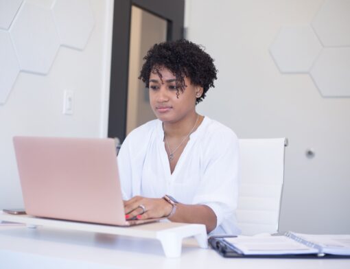 Jovem estudando em um notebook, com caderno aberto ao lado sobre a mesa