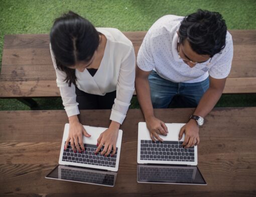 Duas pessoas trabalhando lado a lado em notebooks, vistas de cima