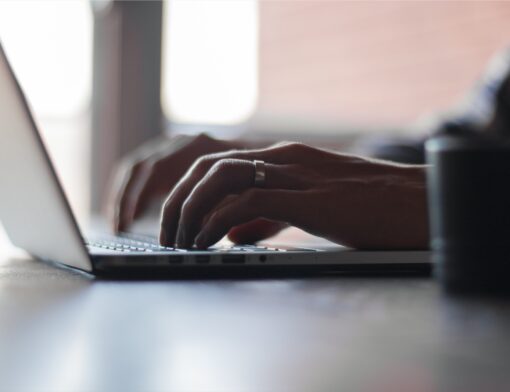Mãos digitando no teclado de um notebook sobre a mesa